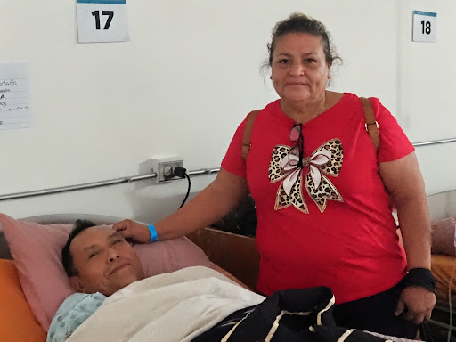 A patient in Guatemala recovering in bed with a family member standing beside him
